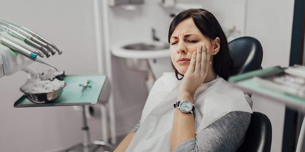 Woman with tooth pain at dentists sat in dental chair fix chipped teeth options