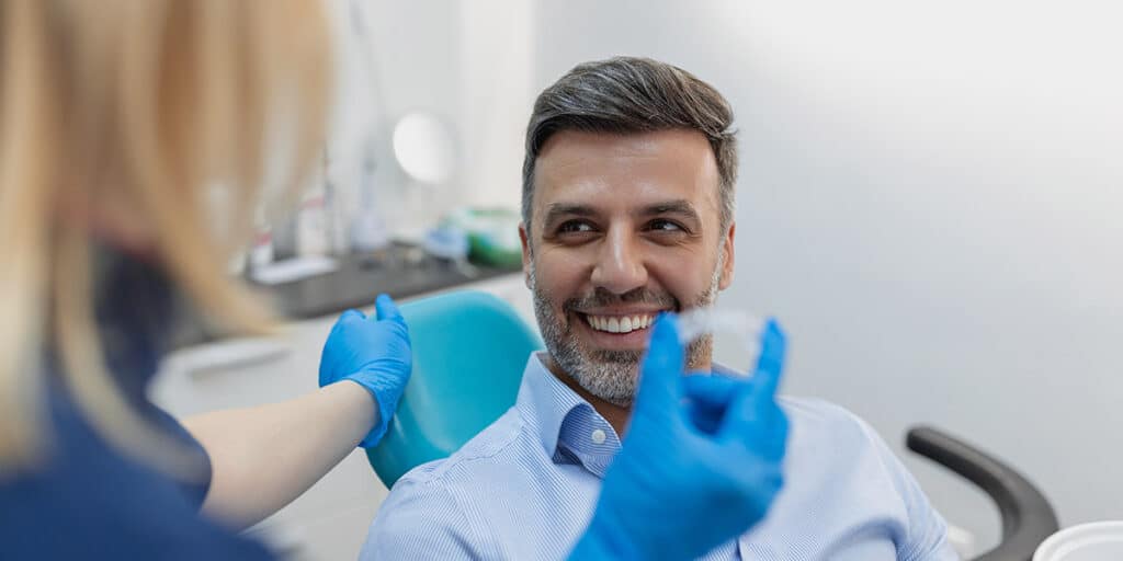 Man smiling at dentiss and can invisalign fix crooked teeth