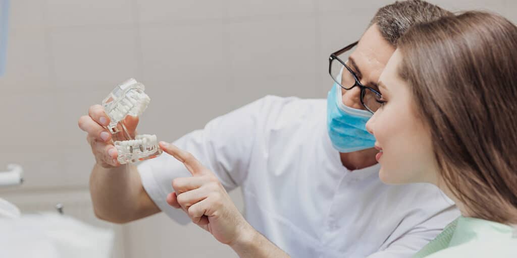 dentist showing woman dental implant model and dental implants cost